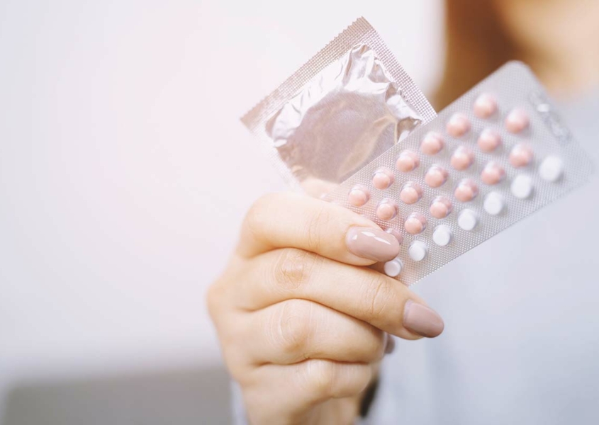 Woman's hand holding birth control pills and a condom
