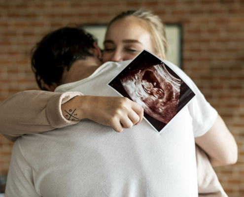 Woman holding ultrasound and hugging partner