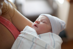 A mother holds her newborn in the hospital bassinet